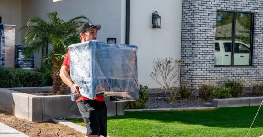 Midas Moving crew member carrying a wrapped furniture item outside a home