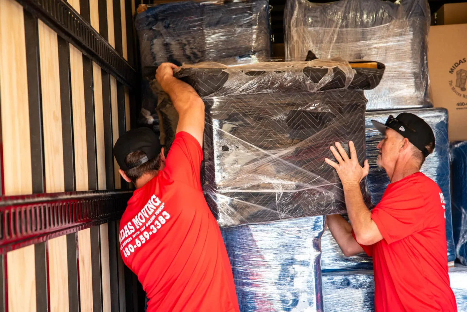 Midas Moving movers loading padded and shrink-wrapped furniture into a moving truck