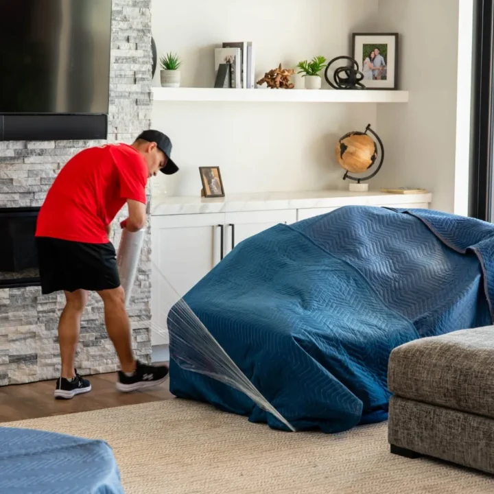 Midas Moving crew member securing a moving blanket around a sofa with stretch wrap in a Gilbert, AZ home