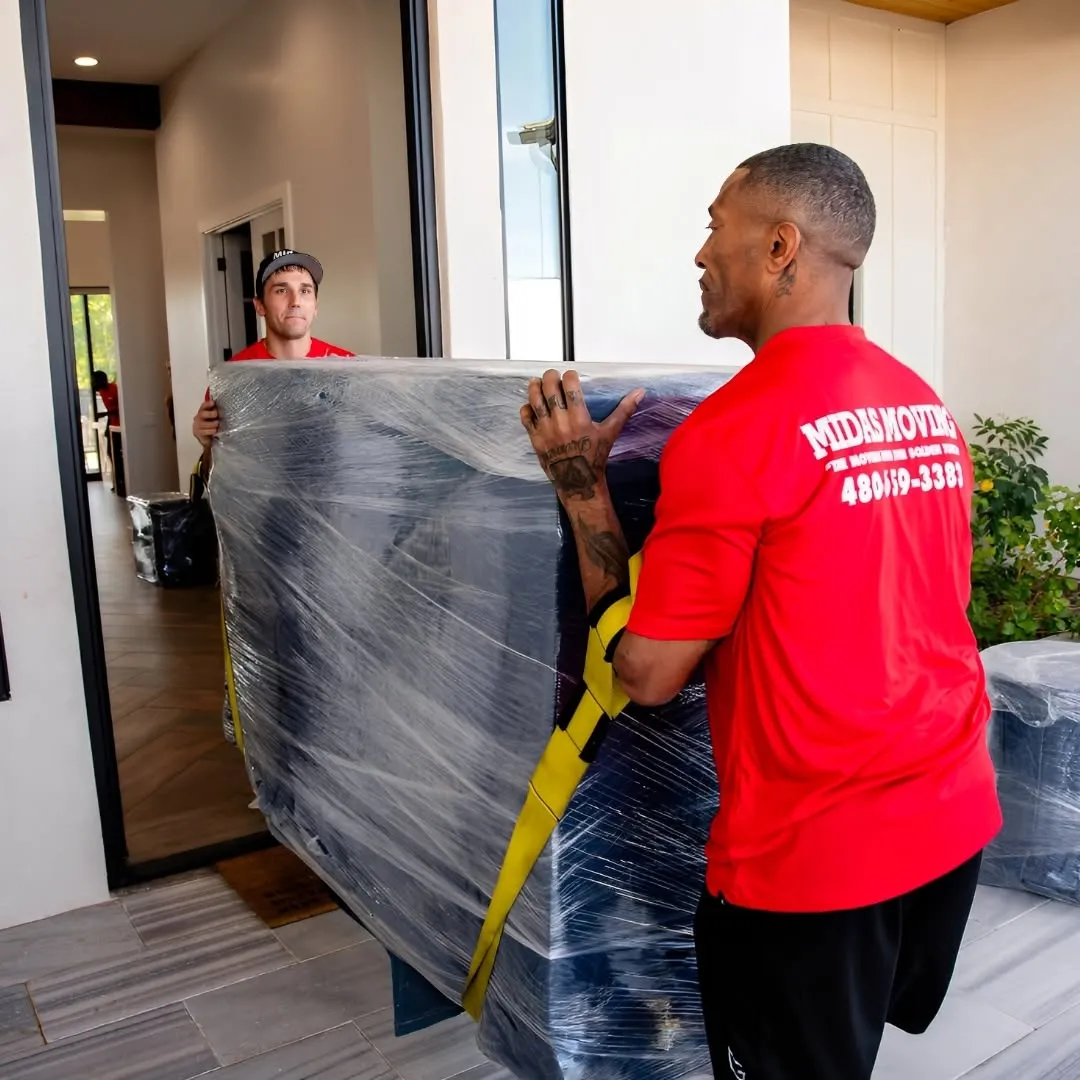 Two Midas Moving crew members using lifting straps to carry wrapped furniture through a doorway