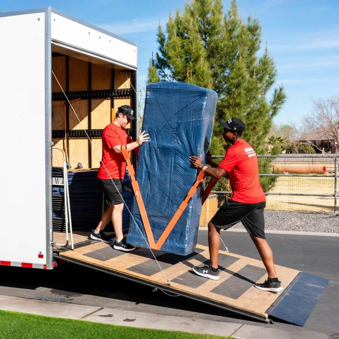 Two Midas Moving crew members using lifting straps to load blanket-wrapped furniture into a moving trailer in Gilbert, AZ