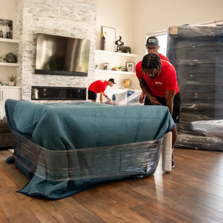 Midas Moving crew wrapping a sofa with moving blankets and stretch wrap inside a home in Gilbert, AZ