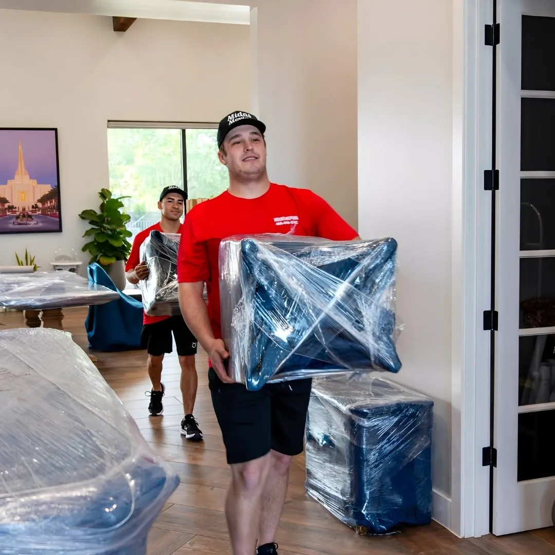 Midas Moving crew carrying plastic-wrapped furniture through a home