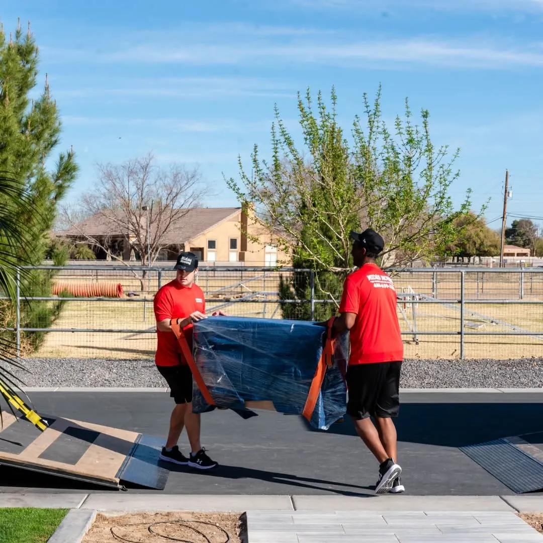 Two Midas Moving crew members using lifting straps to carry wrapped furniture toward a moving truck ramp
