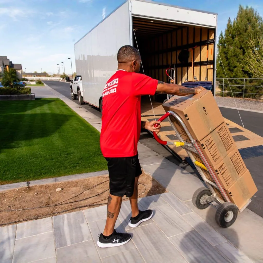Midas Moving crew member using a hand truck to move boxes beside a moving truck