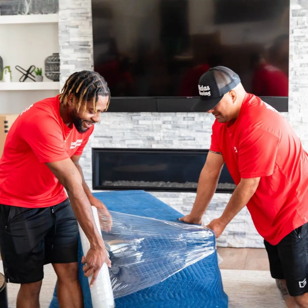 Two Midas Moving crew members wrapping furniture in protective blankets and plastic