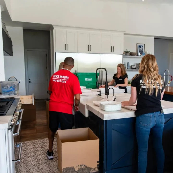 Midas Moving mover carrying a box through a kitchen while the homeowner packs